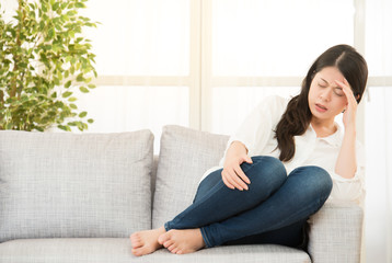 woman suffering headache sitting on sofa