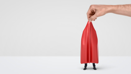 A giant hand taking off a red drapery from a hidden businessman on white background.