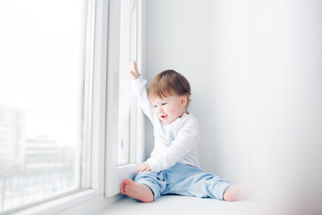 Fototapeta premium Adorable little baby seating on windowsill. looking out the window