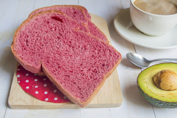 Pink whole wheat bread with espresso coffee and avocado on white woodle.