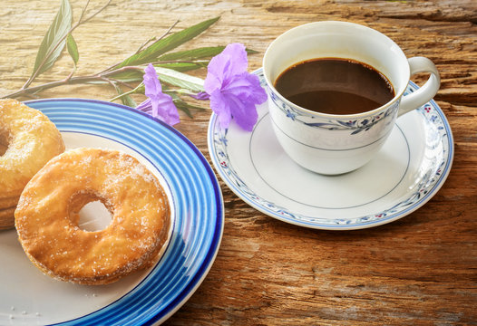 Morning coffee with doughnuts and purple blue flowers on wood background. Soft light effect added.