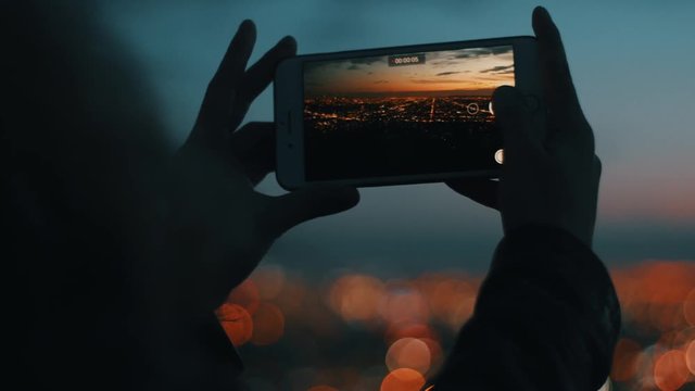 Girl is holding mobile phone and making pictures of city at dusk with nice bokeh.