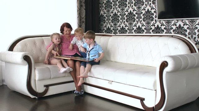 Grandmother with three grandchildren watching a photo album sitting on a leather sofa.