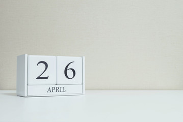 Closeup white wooden calendar with black 26 april word on blurred white wood desk and cream color wallpaper in room textured background with copy space in selective focus at the calendar