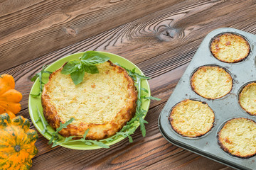 squash casserole decorated by basil leaf and arugula on light green plate at wooden table with squash fruits and light green napkins at white polka dots pattern, pan with squash fritters