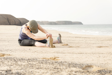 Fototapeta na wymiar Lady Sitting on a Beach Doing Leg Stretches