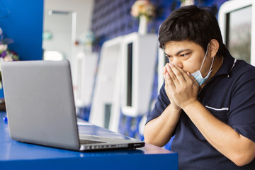 Sick businessman use laptop computer with temperature and headache working in office., Asian man wearing a face mask with coughing