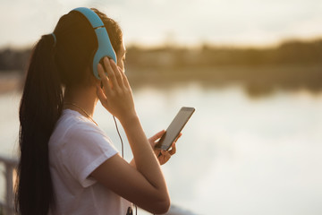 Asian woman listening music at the park with a pond during the evening.