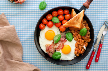 Frying pan with fried egg, beans, tomatoes, bacon and toast