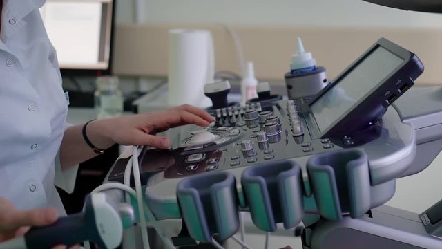 Close up of control board of device for ultrasound diagnostic. Doctor in white scrubs holding transducer in hand and using medical equipment for sonography and scanning visceral organs of patient.