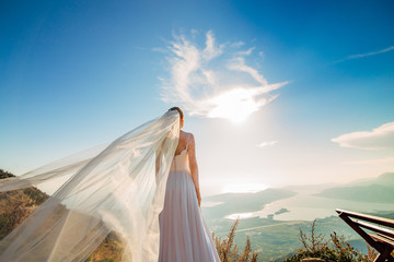 Fototapeta na wymiar Happy beautiful bride outdoors. Wedding dress fluttering in the wind. Building in the background.