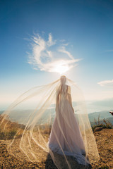Fototapeta na wymiar Happy beautiful bride outdoors. Wedding dress fluttering in the wind. Building in the background.