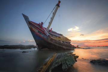 Fototapeta na wymiar Boat deteriorate breaking down laying in the coast side with sunet in background