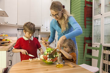 Mother and little child stirring vegetable salad. Kids helping Mom on the kitchen. 