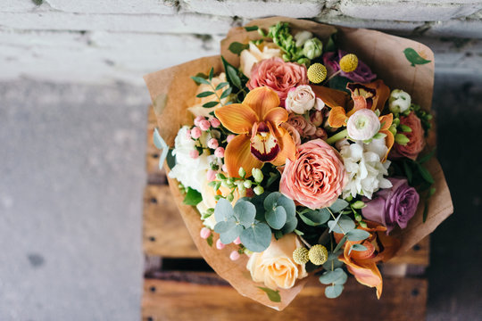 Colorful  bouquet of different fresh flowers against brick wall. Bunch of orchids, roses, freesia and eucalyptus leaves. Rustic flower background