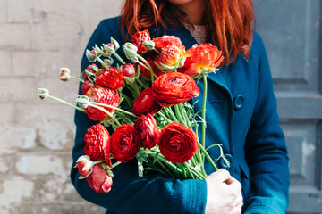 Female hands holding a bouquet of red anunculus  flowers on a rustic background