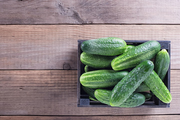 Box with fresh cucumbers on old wooden table top view