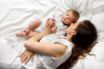 Portrait of a beautiful mother smiling with her 3 month old baby on the bed, top view