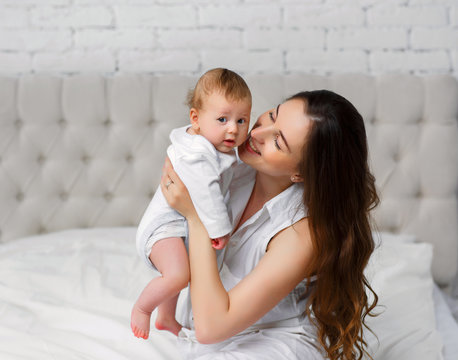 Portrait of beautiful mother holding her 3 month old baby in the bedroom and smiling