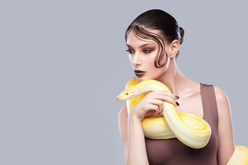 Beautiful brunette woman with a albine python. Fashion makeup, gray background