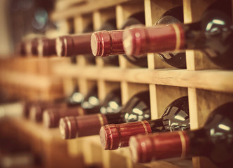 Red wine bottles stacked on wooden racks - obrazy, fototapety, plakaty