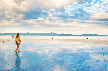A girl walking on top of Sun Salutation installation made of solar photovoltaic cells near the sea...