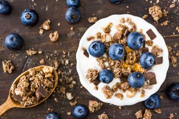 Serving of Yogurt with Whole Fresh Blueberries and Muesli on Old Rustic Wooden Table. Closeup Detail.