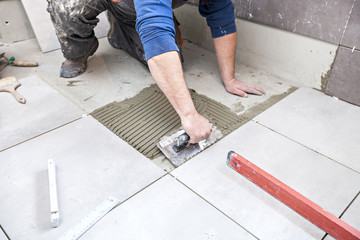 Tiling Floor & Wall. The tiler builder arranges the bathroom ceramics. Laying tiles on the floor