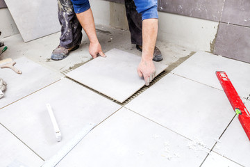 Tiling Floor & Wall. The tiler builder arranges the bathroom ceramics. Laying tiles on the floor