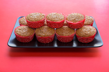 Bran muffins in bright red and white paper holders on a black rectangular plate and red background