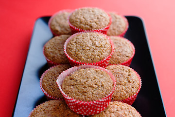 Bran muffins in bright red and white paper holders on a black rectangular plate and red background