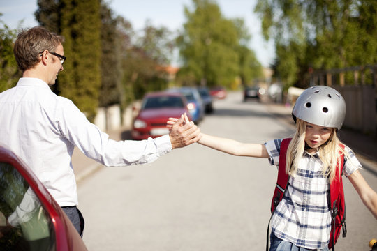 Father and daughter wearing cycling helmet giving high five on street