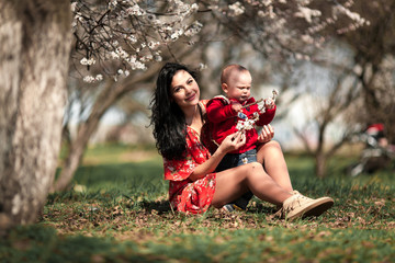 Young mother with her baby on walk in blooming garden.