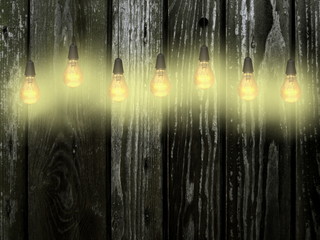 Multiple yellow light bulbs against gray and green weathered wooden boards