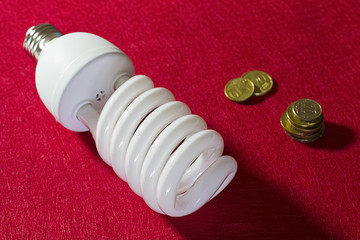 Energy saving light bulb and  coins on red background. Soft focus.