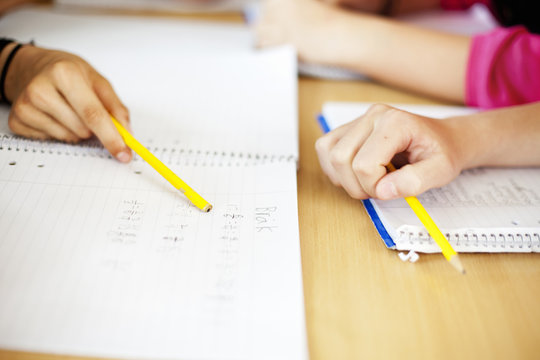 High angle view of students holding pencil over books in classroom