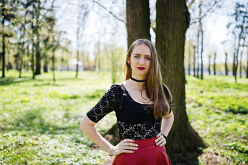 Portrait of girl with bright make up with red lips, black choker necklace on her neck and red leather skirt at spring park.