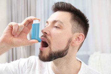 Young man using asthma inhaler at home