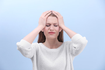 Beautiful young woman suffering from headache on color background