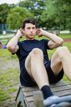 Handsome man practicing sit-ups on bench at park