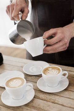Midsection of barista making cappuccino at table in coffee shop