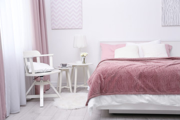 Comfortable bed with soft pink coverlet, pillows and chair in light modern room