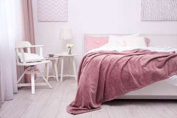 Comfortable bed with soft pink coverlet, pillows and chair in light modern room
