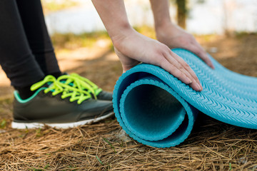 Girl in sports shoes spreads blue karemat in nature, for yoga, warm-up or meditation