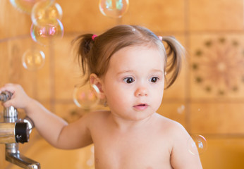 Little girl in bathtub playing with soap bubbles