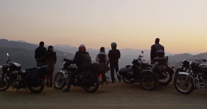 A group of motorcyclists rest and look at the sunset with the Himalayas