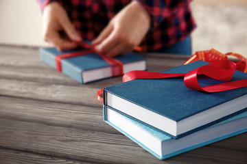 Woman decorating book with ribbon as gift on wooden table