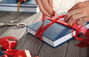 Woman decorating book with ribbon as gift on wooden table
