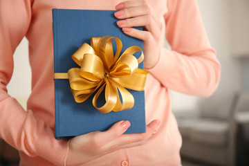 Woman holding book with ribbon as gift on blurred background