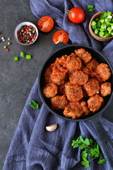 Homemade meatballs with tomato sauce and onions in a frying pan on a concrete background